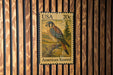 A 20c US postage stamp featuring an American Kestrel bird is displayed on a wooden wall.