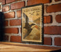 A vintage-style postage stamp featuring a black skimmer bird is displayed on a brick wall.