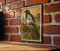 A framed illustration of a black and white bird perched on a branch is displayed on a brick wall.