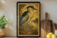 a framed painting of a heron standing on a grassy area, with a wooden cutting board and a potted plant nearby.