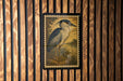 a framed illustration of a bird, likely a heron, displayed on a wooden wall.