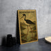 a metal sign with a black and white illustration of a bird, specifically a Black-Necked Stilt, standing on a grassy area near a body of water.