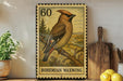 A vintage postage stamp featuring a bohemian waxwing bird, displayed on a wooden shelf next to a potted plant and a wooden cutting board.