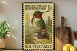A framed vintage postage stamp depicting a broad-tailed hummingbird, with a wooden cutting board and lemons in the background.