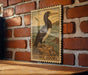 A wooden frame with a postage stamp-like design featuring a brown booby bird perched on a rock, mounted on a brick wall.