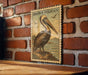 A framed image of a pelican is hanging on a brick wall, with a wooden table below it.