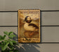 A wooden postcard-style sign with a duck illustration, mounted on a wall.