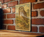 a framed illustration of an owl on a brick wall.