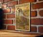 A California Quail postage stamp is displayed on a brick wall, with a wooden table below it.