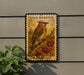 A vintage-style postage stamp featuring a bird perched on a branch with berries, mounted on a wall.