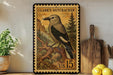 A framed stamp-like artwork depicting a bird, likely Clark's Nutcracker, is displayed on a shelf next to a wooden cutting board and some lemons.