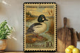 A vintage-style postage stamp depicting a Common Goldeneye duck, with a price of 10 cents, is displayed on a wooden surface next to a wooden cutting board and some lemons.