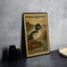 A vintage U.S. postage stamp featuring a Common Goldeneye duck, placed on a dark surface next to some black camera lenses.