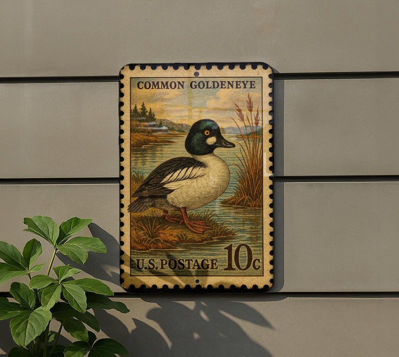 A vintage U.S. postage stamp featuring a Common Goldeneye duck, mounted on a wall next to a plant.