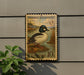 A vintage U.S. postage stamp featuring a Common Goldeneye duck, mounted on a wall next to a plant.