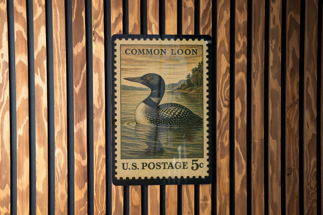 A U.S. postage stamp featuring a loon, a type of bird, is displayed on a wooden wall.
