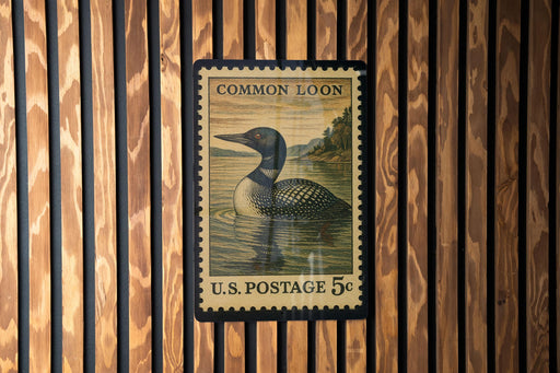 A U.S. postage stamp featuring a loon, a type of bird, is displayed on a wooden wall.