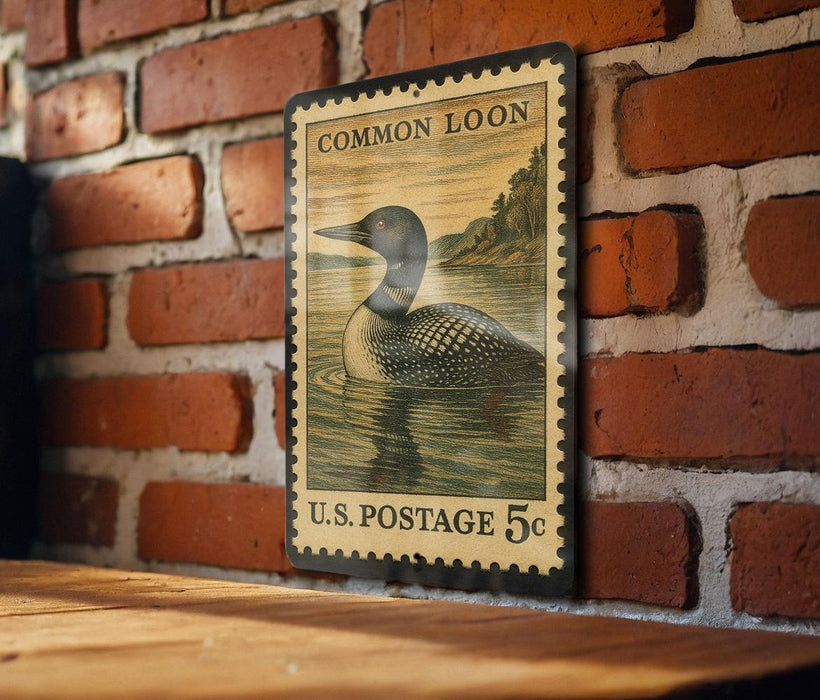 A vintage U.S. postage stamp featuring a loon is displayed on a brick wall.