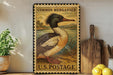 A vintage-style postage stamp featuring a duck is displayed on a shelf, surrounded by kitchen utensils and a potted plant.