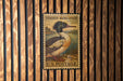 A vintage-style postage stamp featuring a duck is displayed on a wooden wall.