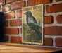 a vintage-style postage stamp with a black raven illustration, mounted on a brick wall.