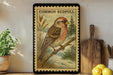 a framed illustration of a Common Redpoll bird perched on a branch, with a vintage stamp-like border.