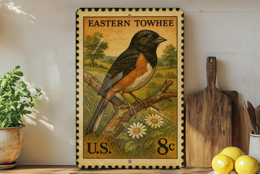 A vintage-style postage stamp featuring a colorful illustration of a bird perched on a branch, with a field and flowers in the background. The stamp is displayed on a shelf next to a wooden cutting board and a potted plant.