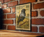 A vintage European postage stamp featuring a black bird perched on a branch, mounted on a brick wall.