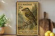 A framed U.S. postage stamp depicting a golden crowned kinglet perched on a branch, with a potted plant and wooden cutting board visible in the background.