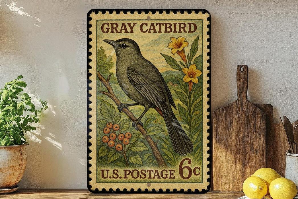 A vintage postage stamp featuring a gray catbird perched on a branch with flowers, placed on a wooden surface next to a wooden cutting board and a potted plant.