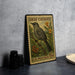 A vintage postage stamp featuring a gray catbird perched on a branch with flowers, placed on a countertop next to some black camera lenses.