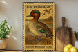 A vintage U.S. postage stamp featuring a green-winged teal duck, displayed on a wooden shelf next to a wooden cutting board and some lemons.