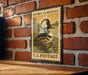 A vintage postage stamp featuring a hooded merganser duck, mounted on a brick wall.