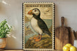 a framed illustration of a horned puffin bird perched on a rocky cliff overlooking the ocean.