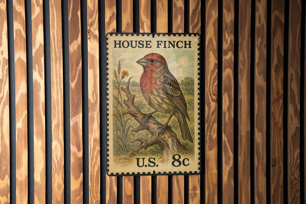 A vintage-style postage stamp featuring a colorful illustration of a finch perched on a branch, mounted on a wooden wall.