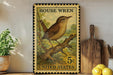 A vintage-style stamp depicting a house wren, with the text "HOUSE WREN" and "5c UNITED STATES" printed on it. The stamp is placed on a shelf next to a wooden cutting board and a potted plant.