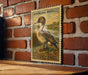 A vintage postage stamp featuring a duck is displayed on a brick wall.