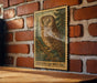 A framed illustration of a Northern Saw-Whet Owl is displayed on a brick wall, with a wooden table below it.