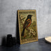 A vintage-style postage stamp featuring an orange and black oriole perched on a branch with white flowers, placed on a gray countertop next to some black camera lenses.