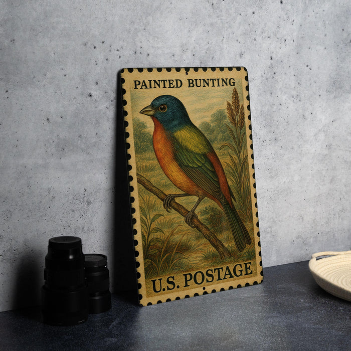 A vintage painted buntings postage stamp featuring a colorful bird perched on a branch, displayed on a table next to some black camera lenses.