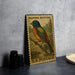 A vintage painted buntings postage stamp featuring a colorful bird perched on a branch, displayed on a table next to some black camera lenses.