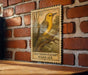 a wooden table with a framed illustration of a yellow bird perched on a branch, mounted on a brick wall.
