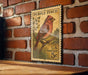 A vintage purple finch postage stamp is displayed on a brick wall, with a wooden table below it.