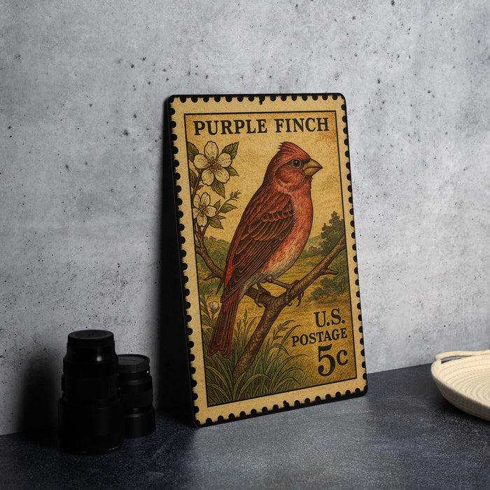 A vintage Purple Finch postage stamp from the U.S. is displayed on a table, featuring a detailed illustration of the bird perched on a branch with flowers.