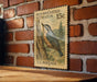 A vintage U.S. postage stamp featuring a nuthatch perched on a tree, mounted on a brick wall.