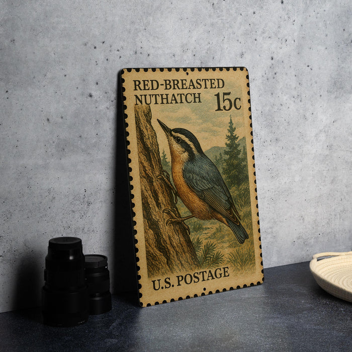 A vintage U.S. postage stamp featuring a red-breasted nuthatch, placed on a dark surface next to some black camera lenses.