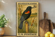 A framed vintage postage stamp depicting a blackbird, with a price of 8 cents, is displayed on a shelf next to a wooden cutting board and some lemons.