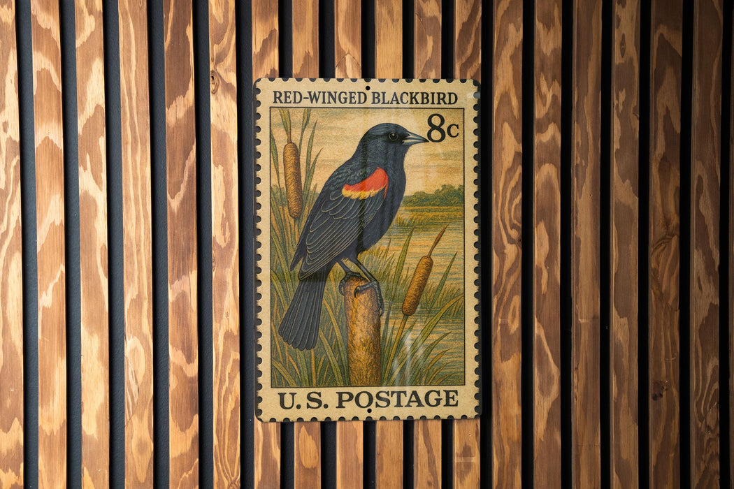 A U.S. postage stamp featuring a black bird with red and orange markings, standing on a cattail plant.