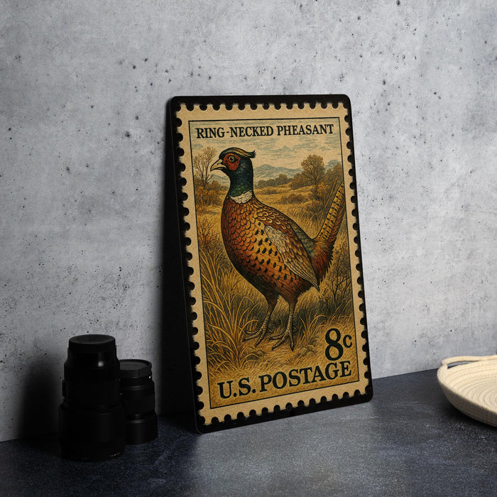 A metal postage stamp featuring a pheasant standing in a field, with the text "Ring-Necked Pheasant" and "U.S. Postage" printed on it.