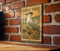 A vintage-style postage stamp featuring a detailed illustration of a bird, likely a tern, is displayed on a brick wall.